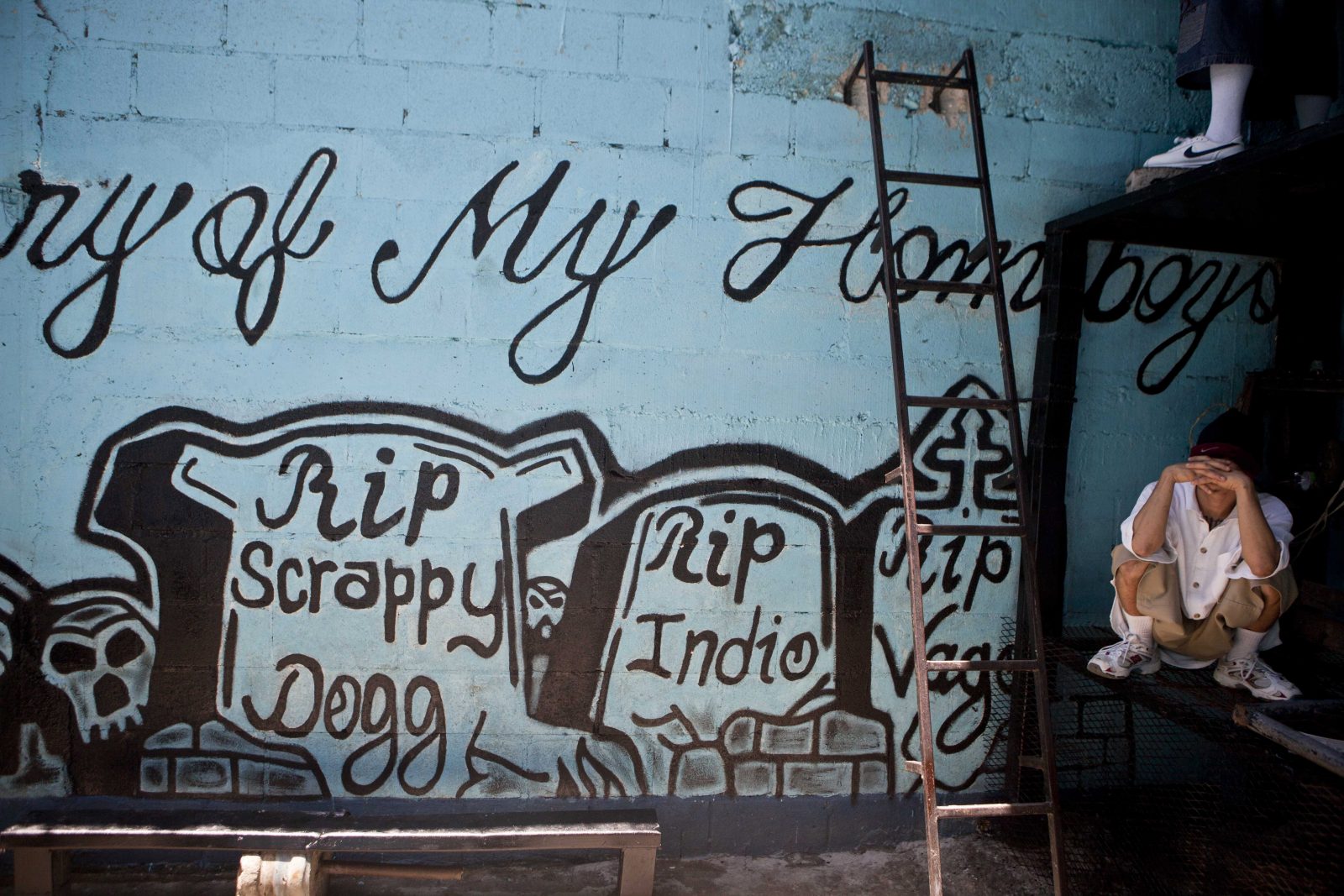 An 18 Street gang member sits near a mural on the sidelines of a press conference inside the San Pedro Sula prison in Honduras, Tuesday, May 28, 2013. Honduras' largest and most dangerous street gangs have declared a truce, offering the government peace in exchange for rehabilitation and jobs. A Mara Salvatrucha spokesman says the gang and a rival known as 18th Street will commit to zero violence and zero crime in the streets as first step show of good faith. (AP Photo/Esteban Felix)