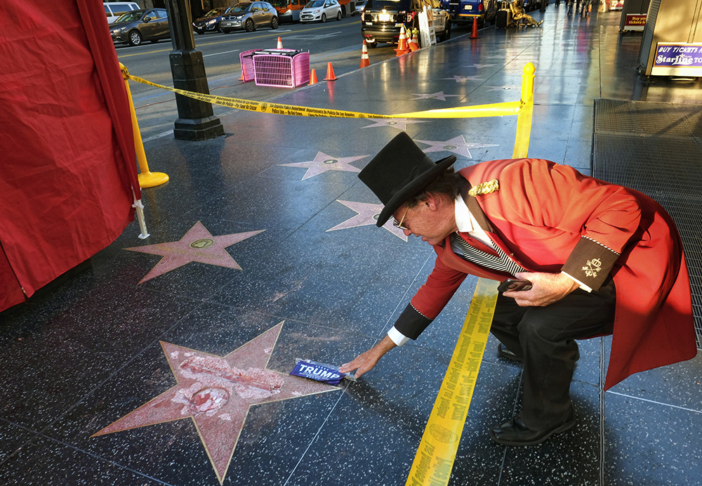 Gregg Donovan, who calls himself the unofficial ambassador of Hollywood, places a sticker for Republican presidential candidate Donald Trump on Trump's vandalized star on the Hollywood Walk of Fame, Wednesday, Oct. 26, 2016 in Los Angeles. Det. Meghan Aguilar said investigators were called to the scene before dawn Wednesday following reports that Trump's star was destroyed by blows from a hammer. (AP Photo/Richard Vogel)